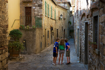 Three unidentifiable children with their backs to the camera, playing in a deserted street in the beautiful village of Montefioralle, Tuscany, Italy