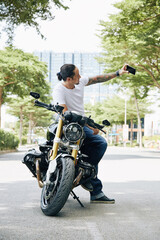 Obraz premium Proud happy fit man taking selfie next to his motorcycle after ride to upload on social media