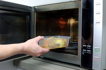 person preparing food in oven. reheating in a microwave oven
