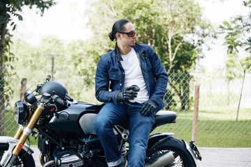 Fototapeta na wymiar Handsome stylish man sitting on motorcycle with cup of take out coffee and looking away