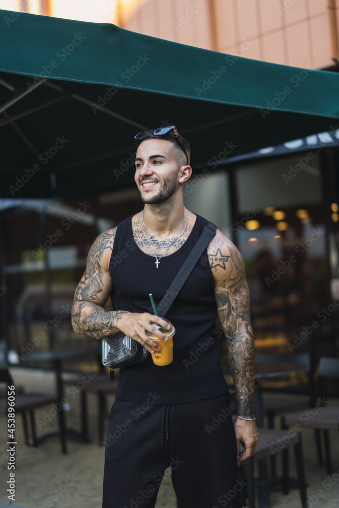 Canvas Prints young smiling caucasian guy with cool tattoos holding a cup of juice standing on the street