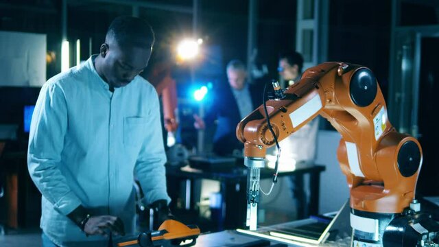Laboratory robot is being operated by an african-american engineer