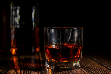 Glass and bottle of cold whiskey on dark background