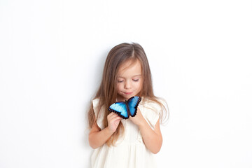A cute little girl holds a live morpho butterfly in her hands and looks at her gently. Emotional portrait on a white background. Care for nature. Childhood. © Анна Брусницына
