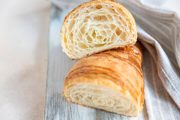 Cut in half croissant with inside texture and thin crisp layers on wooden board, light concrete...