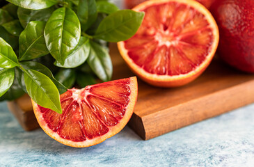Sliced and whole ripe juicy Sicilian blood oranges on wooden cutting board with mint, blue concrete...