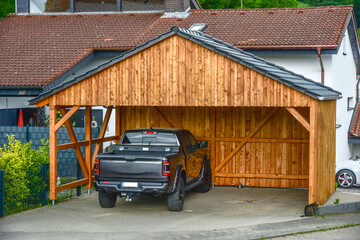 Moderner Carport aus lasiertem/lackiertem Holz im Einfahrtsbereich eines Wohnhauses