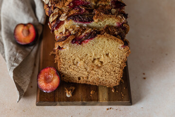 Homemade spicy plum cake decorated with almond on a wooden serving board, concrete background. Loaf cake with plum, spices and almond.