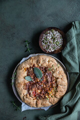 Savory tomato tart, open pie or galette with tomatoes and cheese decorated with aromatic herbs on green background. Top view.