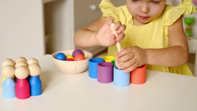 The child holds a wooden spoon with a ball in his hands, which he later throws into a cup of the same color. A girl learns colors by playing a sorter toy. Modern exciting games for preschool education