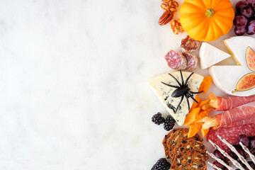 Halloween charcuterie side border against a white marble background. Different cheese and meat appetizers. Copy space.