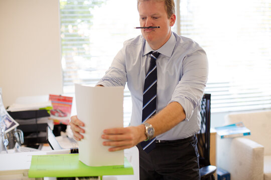 Businessman Holding Stack Of Paper In Office