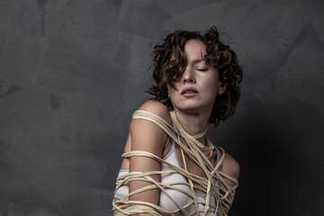Beautiful woman wrapped in a rope over grey wall