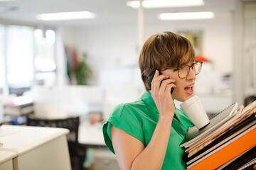 Businesswoman with folders talking on cell phone