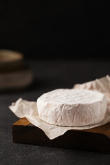 Brie cheese on a wooden board. A piece of camembert. French cuisine. An aperitif on a dark...