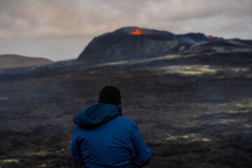 View of a person contemplating the exploding red lava from the Active Volcano in Iceland