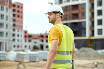 Serious worker in a hardhat and a vest looking away