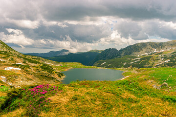Beautiful view of a glacial lake in the mountains under cloudy sky. View of Bucura lake located in Retezat mountains in Romania. View of a mountain lake in a rainy day.