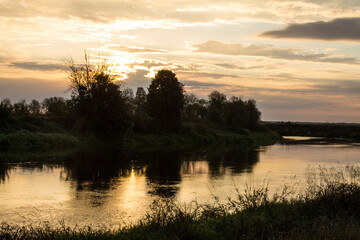A beautiful sunrise over the river and black silhouettes of trees against the background of a cloudy dramatic sky in the early summer morning and a space to copy