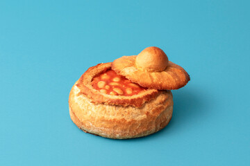 Baked beans in a bread bowl isolated on a blue background.