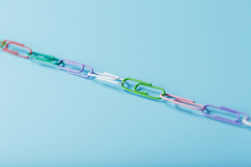 Interlocked colored paper clips in a line on a blue background with free space