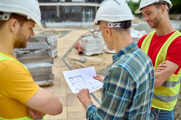 Three Caucasian men in protective helmets studying building plans