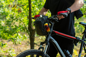 A cyclist in gloves near a mountain bike with a bag on the handlebars.