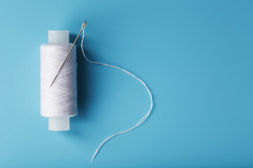 A spool of white thread with a needle on a blue background.