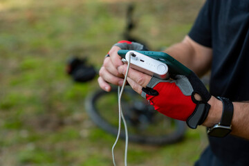 Naklejka premium Man charges a smartphone with a power bank on the background of a bicycle in the forest.