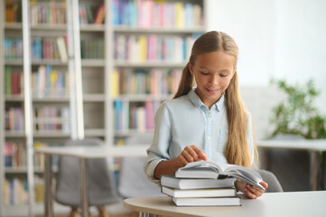 Pleased schoolgirl concentrated on reading a book