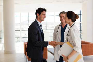 Fototapeta na wymiar Doctor and businessman handshaking in hospital lobby