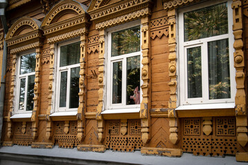 Old historical wooden house in Russian style with carved platbands and a figurine of a pig looking out of the window