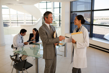 Doctor and businessman handshaking in hospital lobby