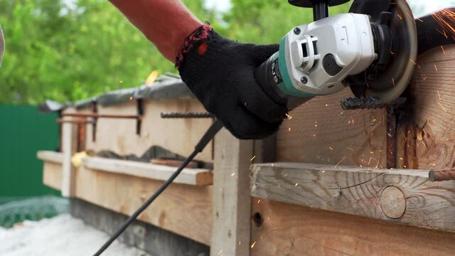 A worker is cutting an extra or needless piece of a steel reinforcing with an angle-grinder. Bright sparks. Working at a house foundation site