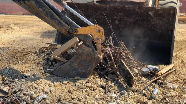 Backhoe bucket loader loads scrap metal into the bucket of the wheel loader. Scrap metal removal from construction site.