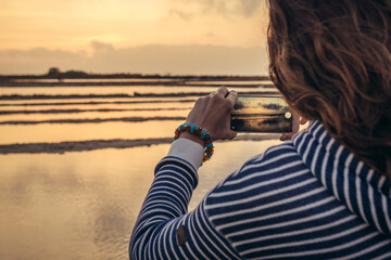 Woman takes photo of a sunset over Saline di Nubia - saltworks in Nubia village near Trapani city,...