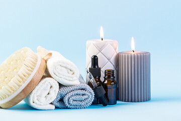 Spa and wellness concept. Rolled towels, essential oils, massage brush and candles on light blue background close up. Skin care procedures. 