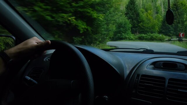 Close up of unrecognizable young man drive camper van or delivery truck on winding mountain road between the trees near calm green forest at sunny day. Man drives car, hold hands on steering wheel