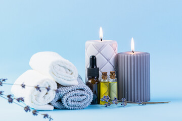  Spa and wellness concept. Rolled towels, essential oils, massage brush and candles on light blue background close up. Skin care procedures.