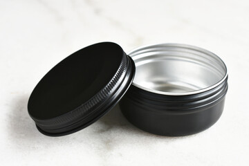 An image of a single black metal container on a white marble table top. 