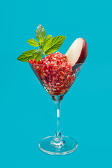Healthy pomegranate seeds in cocktail glass with apple and mint on blue background