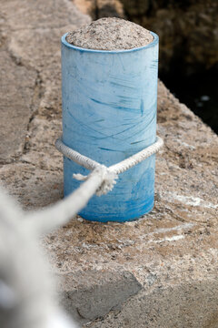Bollard with rope and knot on the harbor quay, close up.