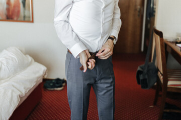 Groom getting ready,  putting on a belt on his wedding day