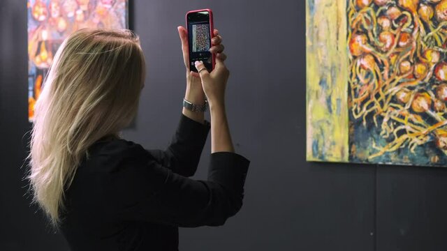 guest of exhibition of modern artist is taking photo by smartphone of picture