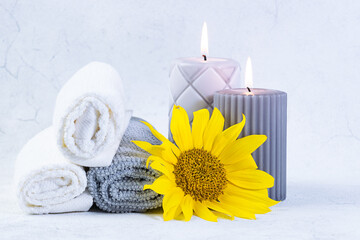 Spa and wellness concept rolled towels, candles and bright yellow sunflower on grey marble background close up. Skin care concept.