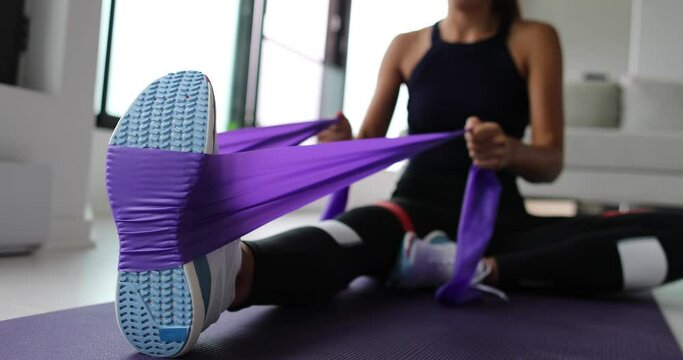 Resistance band exercise at home. Woman doing pilates workout using elastic strap pulling with arms for shoulder training on yoga mat indoors.