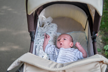 A baby aged one month is lying asleep in a carriage. Caucasian boy child lies in a stroller during...