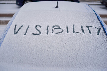 Visibility word on frozen glass of car. Winter car season concept, glass covered with snow. Extreme weather for drivers and transport system. First snow on car window, winter background