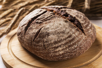 Freshly baked homemade rye black bread on wooden table. Spikelets of rye in a background.