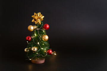Toy christmas tree with balls on a black background with a garland. Cute holiday decor in a dark style.